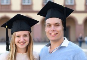 Eine Studienabsolventin und ein Studienabsolvent stehen auf dem Ehrenhof